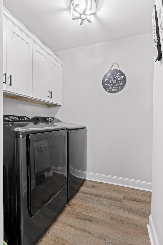 clothes washing area with cabinets, light hardwood / wood-style flooring, and washing machine and clothes dryer