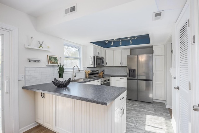 kitchen with kitchen peninsula, appliances with stainless steel finishes, sink, backsplash, and white cabinets