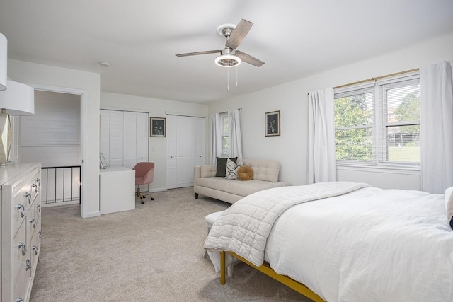 bedroom with ceiling fan, light colored carpet, and two closets