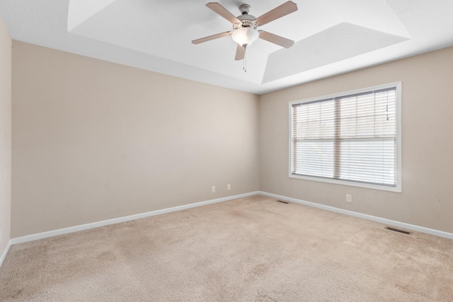 carpeted empty room with ceiling fan and a tray ceiling