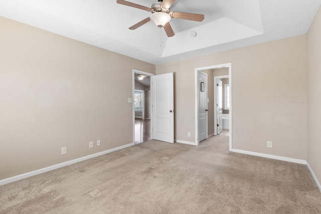 unfurnished bedroom with ceiling fan, ensuite bath, light carpet, and a raised ceiling