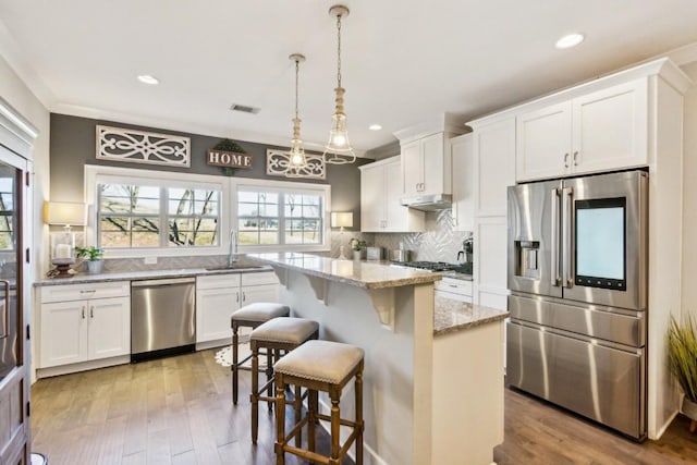 kitchen with white cabinets, a kitchen island, stainless steel appliances, sink, and hanging light fixtures