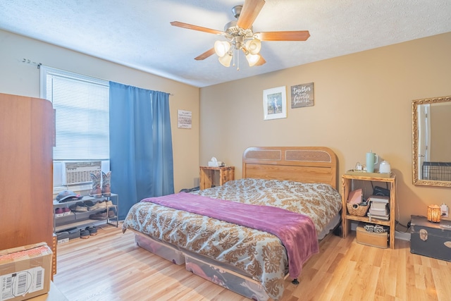 bedroom featuring light wood-type flooring, a textured ceiling, cooling unit, and ceiling fan