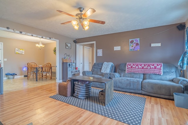 living room with light wood-type flooring, ceiling fan with notable chandelier, and a textured ceiling