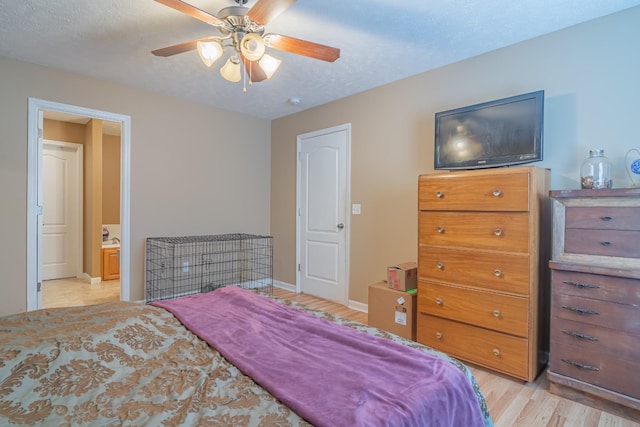 bedroom with ceiling fan, light hardwood / wood-style floors, a textured ceiling, and connected bathroom