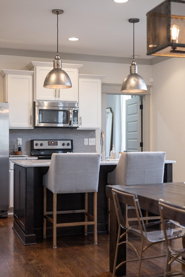 kitchen with backsplash, white cabinetry, hanging light fixtures, and appliances with stainless steel finishes