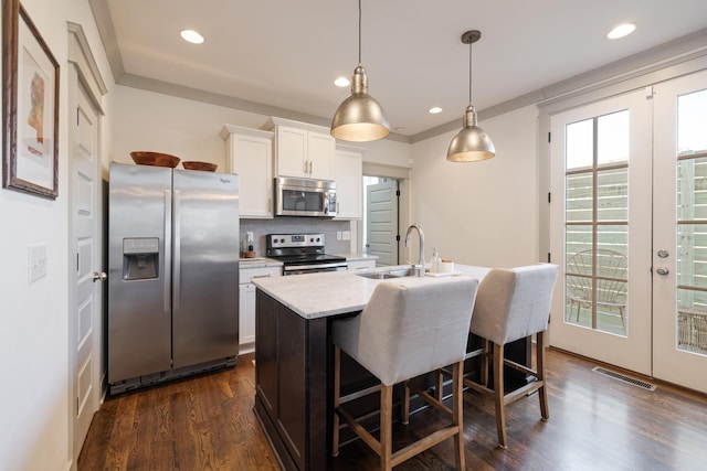 kitchen with french doors, sink, appliances with stainless steel finishes, white cabinetry, and an island with sink