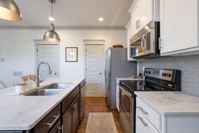 kitchen featuring white cabinets, appliances with stainless steel finishes, decorative light fixtures, sink, and a center island with sink