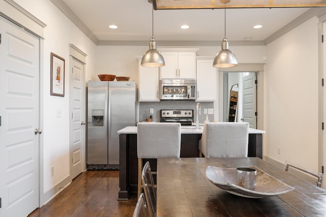 kitchen featuring appliances with stainless steel finishes, decorative light fixtures, white cabinetry, tasteful backsplash, and a kitchen island with sink