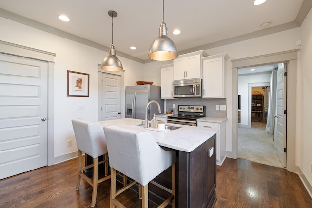 kitchen featuring pendant lighting, appliances with stainless steel finishes, white cabinetry, an island with sink, and sink