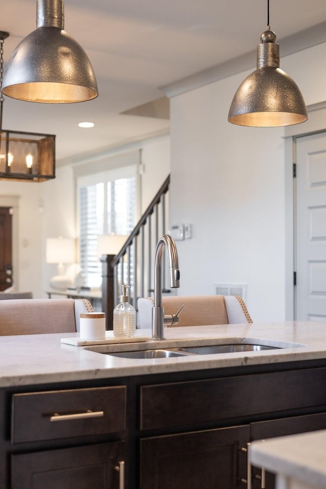 kitchen with sink, decorative light fixtures, dark brown cabinets, and light stone countertops