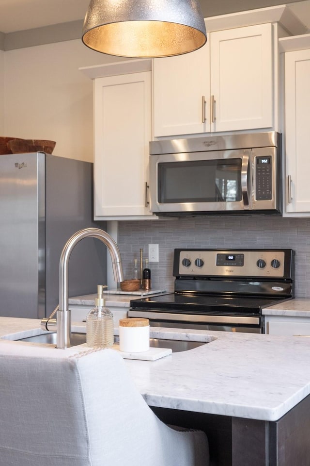 kitchen with decorative backsplash, light stone counters, white cabinets, and stainless steel appliances