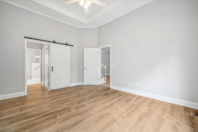 unfurnished bedroom with ceiling fan, a towering ceiling, light hardwood / wood-style flooring, and a barn door