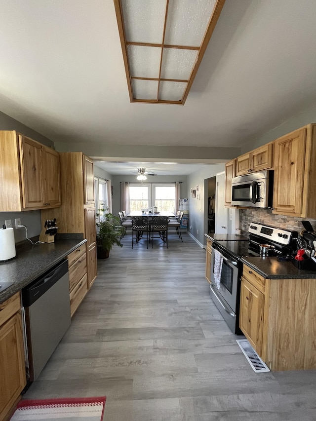 kitchen with ceiling fan, backsplash, stainless steel appliances, and light wood-type flooring