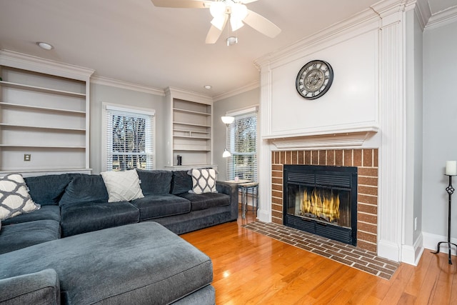 living room with crown molding, a brick fireplace, built in features, hardwood / wood-style flooring, and ceiling fan