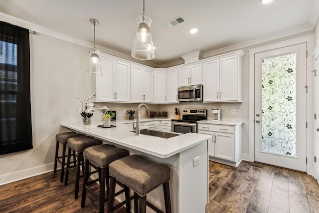 kitchen with appliances with stainless steel finishes, decorative light fixtures, white cabinetry, sink, and kitchen peninsula