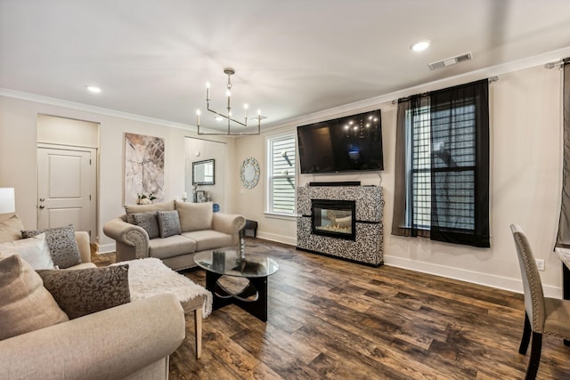 living room featuring a tiled fireplace, dark wood-type flooring, an inviting chandelier, and ornamental molding