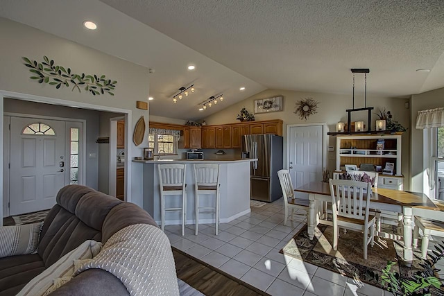 interior space featuring stainless steel fridge with ice dispenser, lofted ceiling, a breakfast bar area, hanging light fixtures, and kitchen peninsula