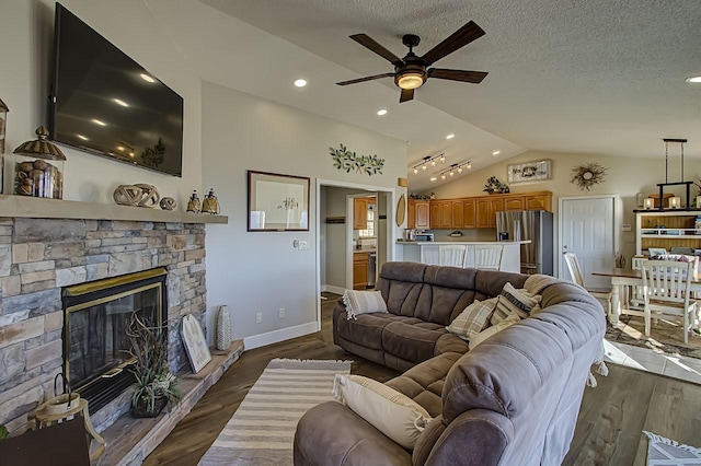 living room with a stone fireplace, vaulted ceiling, a textured ceiling, dark hardwood / wood-style flooring, and ceiling fan