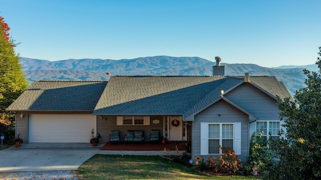 ranch-style home with a porch, a garage, a mountain view, and a front yard