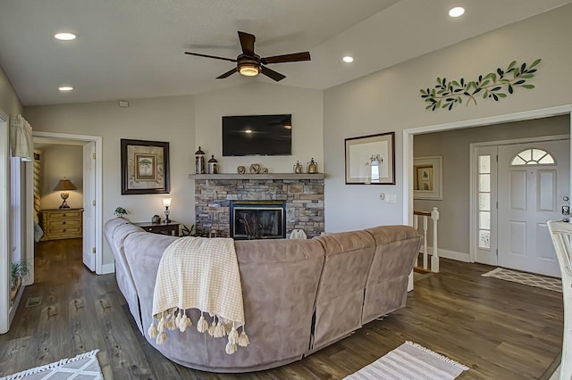 living room featuring dark hardwood / wood-style flooring, vaulted ceiling, and a stone fireplace