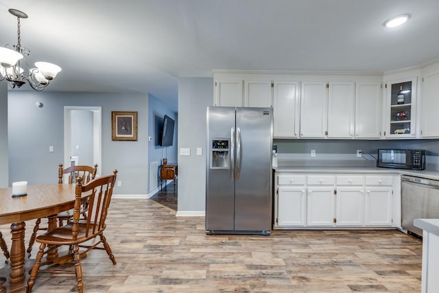 kitchen featuring white cabinets, appliances with stainless steel finishes, hanging light fixtures, a notable chandelier, and light hardwood / wood-style flooring