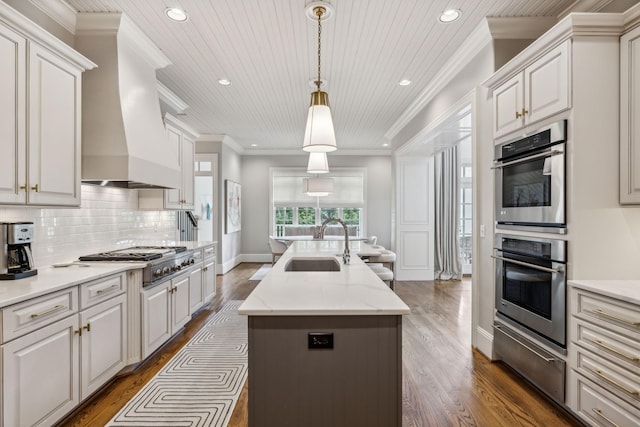 kitchen featuring custom exhaust hood, decorative light fixtures, an island with sink, sink, and dark hardwood / wood-style floors