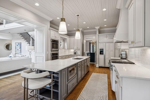 kitchen featuring built in appliances, custom exhaust hood, sink, pendant lighting, and backsplash