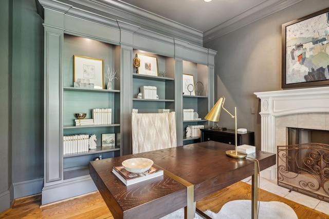 office space featuring built in shelves, ornamental molding, a tile fireplace, and hardwood / wood-style floors