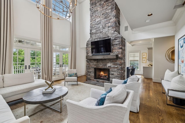 living room featuring a notable chandelier, a towering ceiling, hardwood / wood-style floors, a fireplace, and french doors