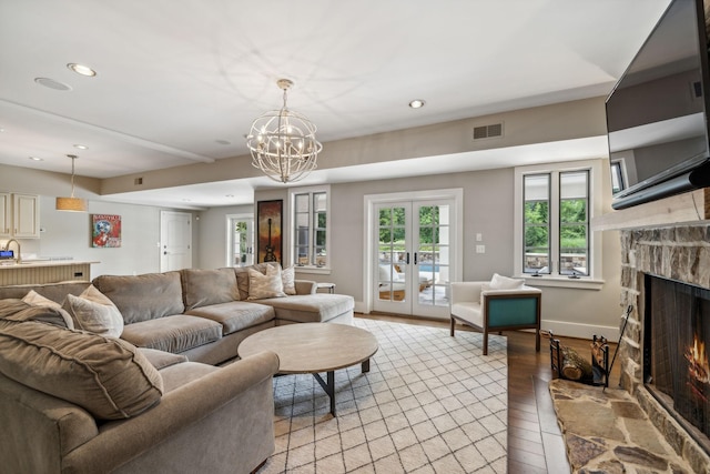 living room featuring a fireplace, light hardwood / wood-style floors, an inviting chandelier, and french doors