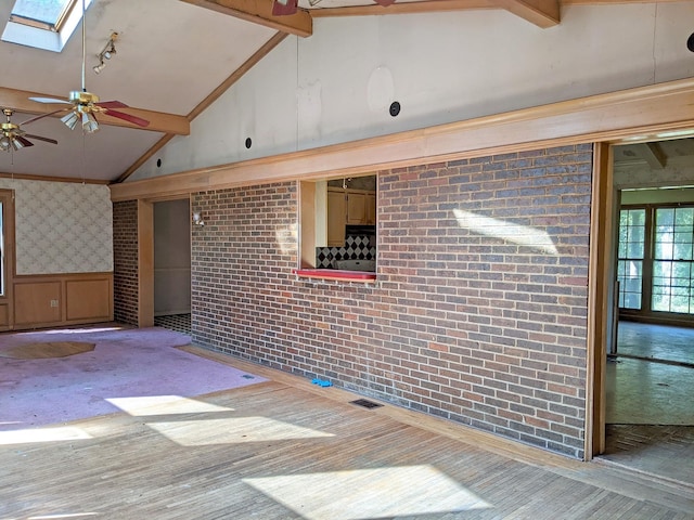 unfurnished room featuring a skylight, brick wall, high vaulted ceiling, beam ceiling, and ceiling fan