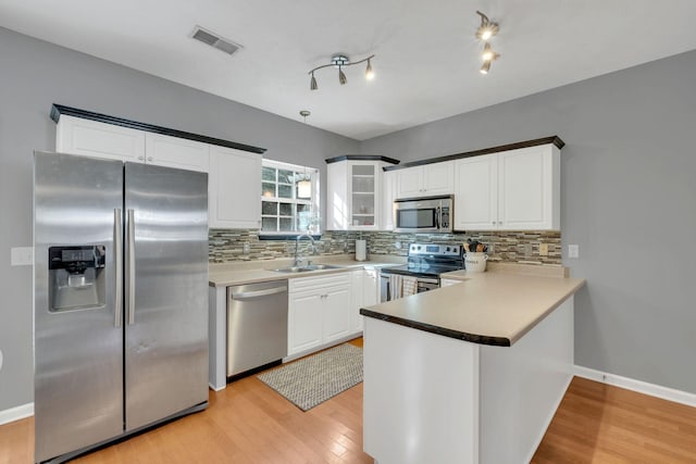 kitchen with appliances with stainless steel finishes, white cabinetry, sink, kitchen peninsula, and light hardwood / wood-style flooring