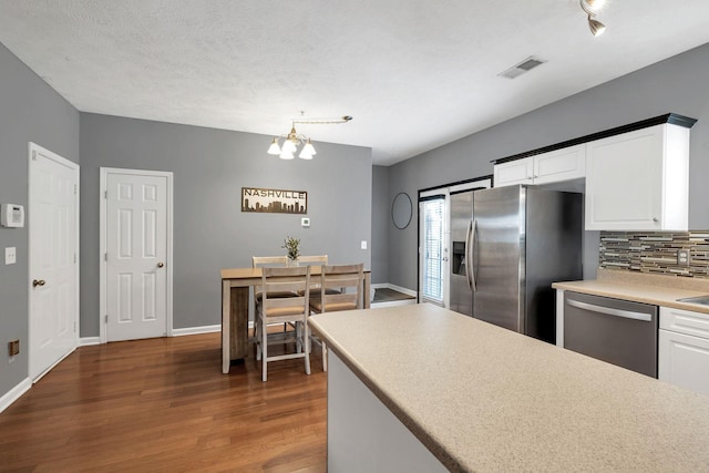 kitchen with white cabinets, appliances with stainless steel finishes, backsplash, dark hardwood / wood-style floors, and a chandelier