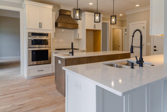 kitchen with premium range hood, white cabinetry, a kitchen island with sink, pendant lighting, and double oven