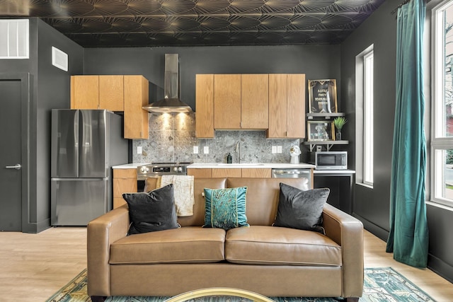 kitchen with a wealth of natural light, sink, backsplash, stainless steel appliances, and wall chimney exhaust hood