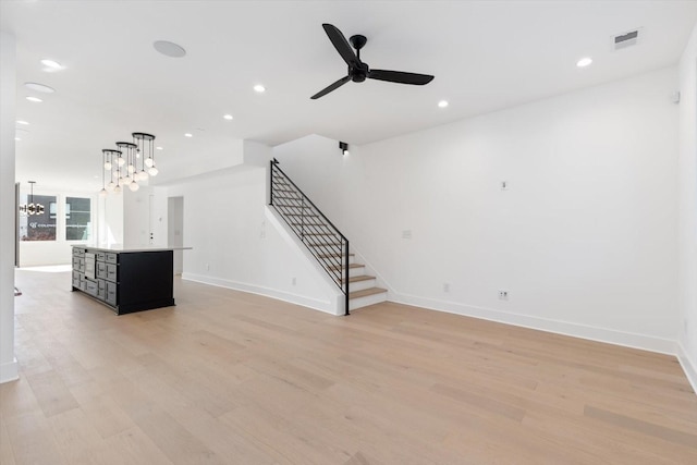 unfurnished living room featuring ceiling fan with notable chandelier and light hardwood / wood-style flooring