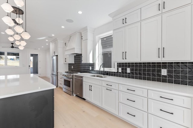 kitchen featuring pendant lighting, white cabinets, high end appliances, sink, and custom range hood