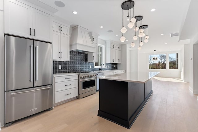 kitchen with premium range hood, hanging light fixtures, white cabinets, a kitchen island, and high quality appliances