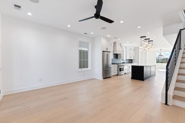 unfurnished living room with light wood-type flooring and ceiling fan with notable chandelier