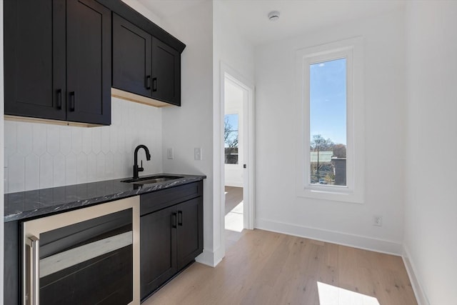 kitchen with light hardwood / wood-style flooring, wine cooler, sink, tasteful backsplash, and dark stone counters