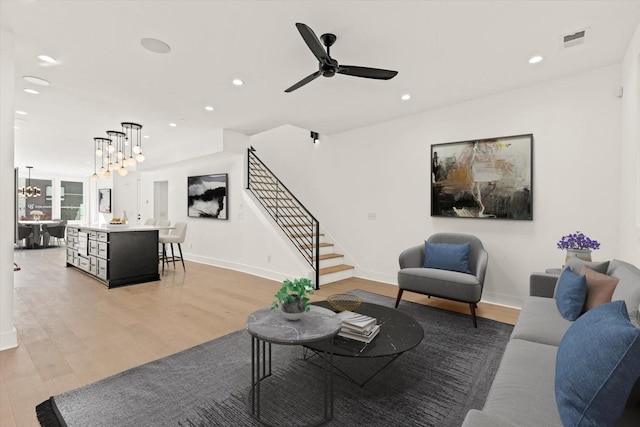 living room featuring ceiling fan with notable chandelier and light hardwood / wood-style flooring