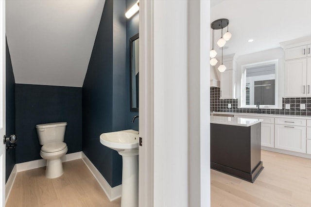 bathroom with lofted ceiling, wood-type flooring, sink, backsplash, and toilet