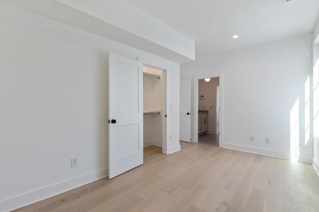 unfurnished bedroom featuring light hardwood / wood-style flooring, a closet, ensuite bath, and a spacious closet