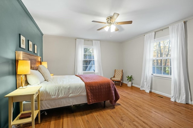 bedroom featuring ornamental molding, ceiling fan, light hardwood / wood-style flooring, and multiple windows