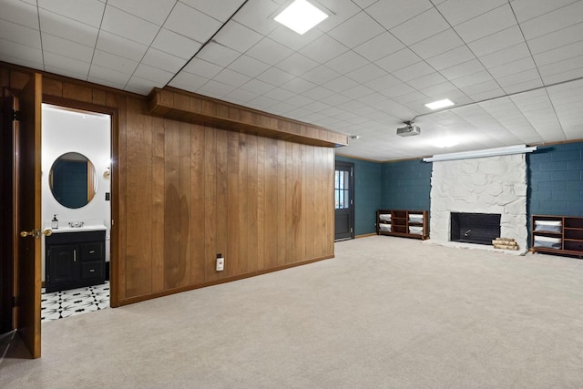 basement featuring a stone fireplace, wood walls, and light colored carpet