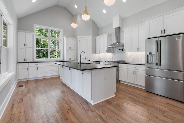 kitchen with wall chimney range hood, white cabinets, premium appliances, and pendant lighting