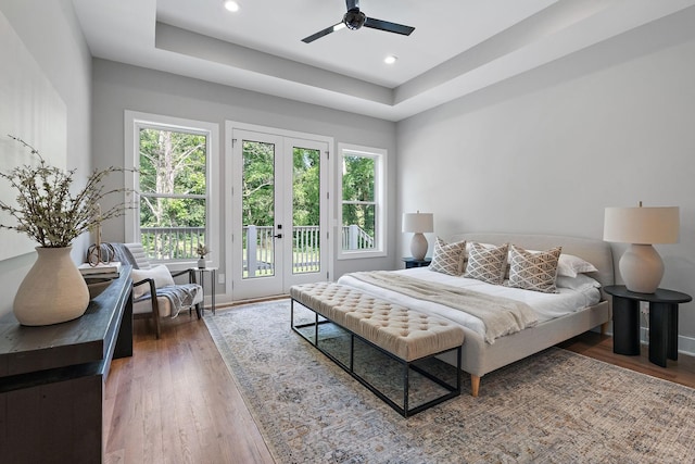 bedroom with ceiling fan, dark hardwood / wood-style floors, a tray ceiling, and access to outside