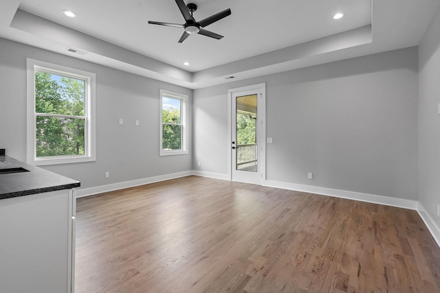 unfurnished living room with hardwood / wood-style flooring, a wealth of natural light, and a tray ceiling