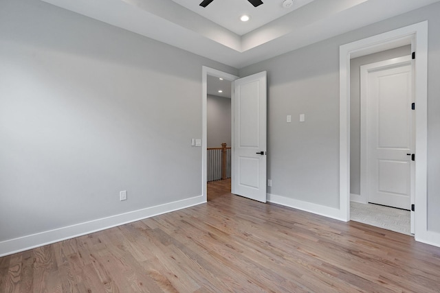 unfurnished bedroom with ceiling fan, light hardwood / wood-style floors, and a raised ceiling